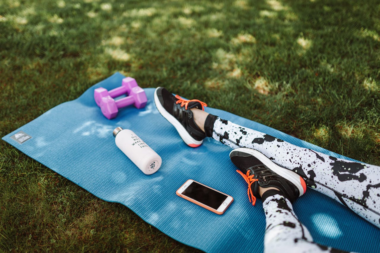 class-03 Focused workout setup outdoors with mat, dumbbells, phone, and water bottle.