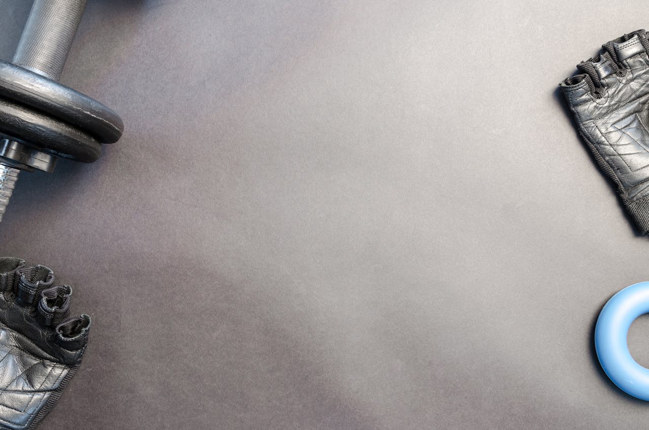 gallery-01 A flat lay of gym essentials including a dumbbell, gloves, and a fitness ring on a neutral background.