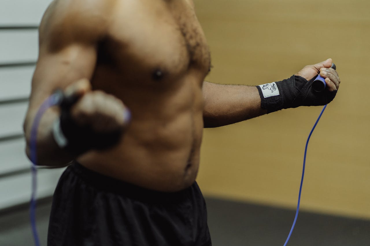 class-02 Focused shirtless man exercising with a jump rope indoors, emphasizing fitness and discipline.
