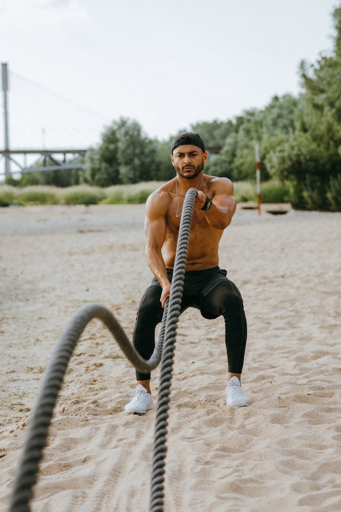 gallery-02 Fit man exercising with battle ropes on a sandy beach, showcasing strength and endurance.