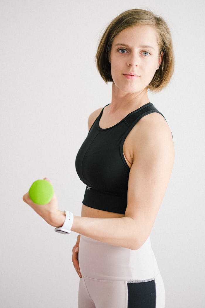 gallery-04 Strong woman exercising indoors with a green dumbbell, promoting healthy lifestyle.